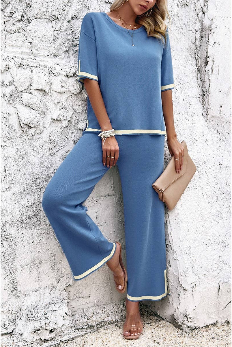 Woman wearing a blue outfit with white trim against a textured white wall.