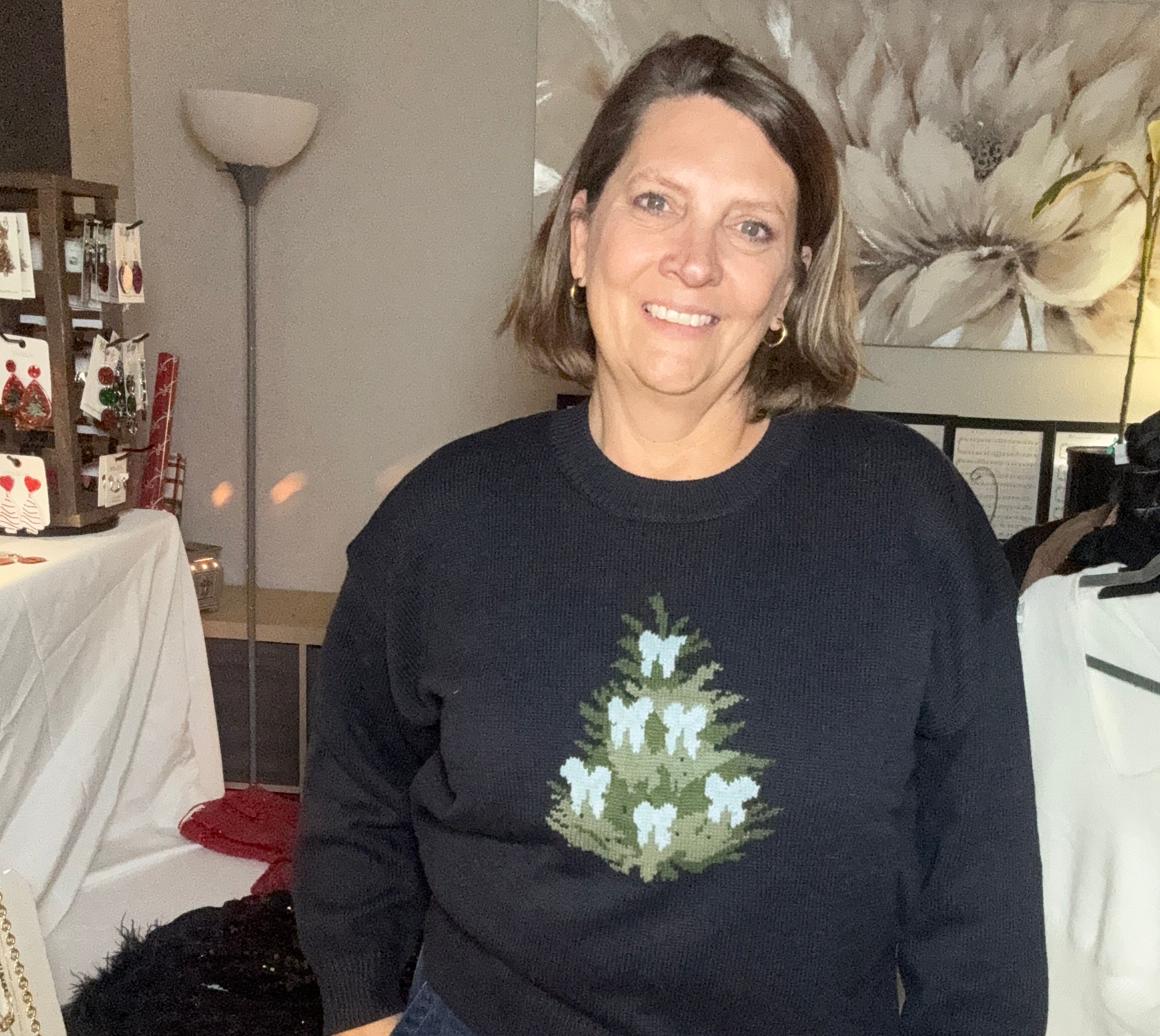 Person wearing a black sweater with a Christmas tree design in a room setting.