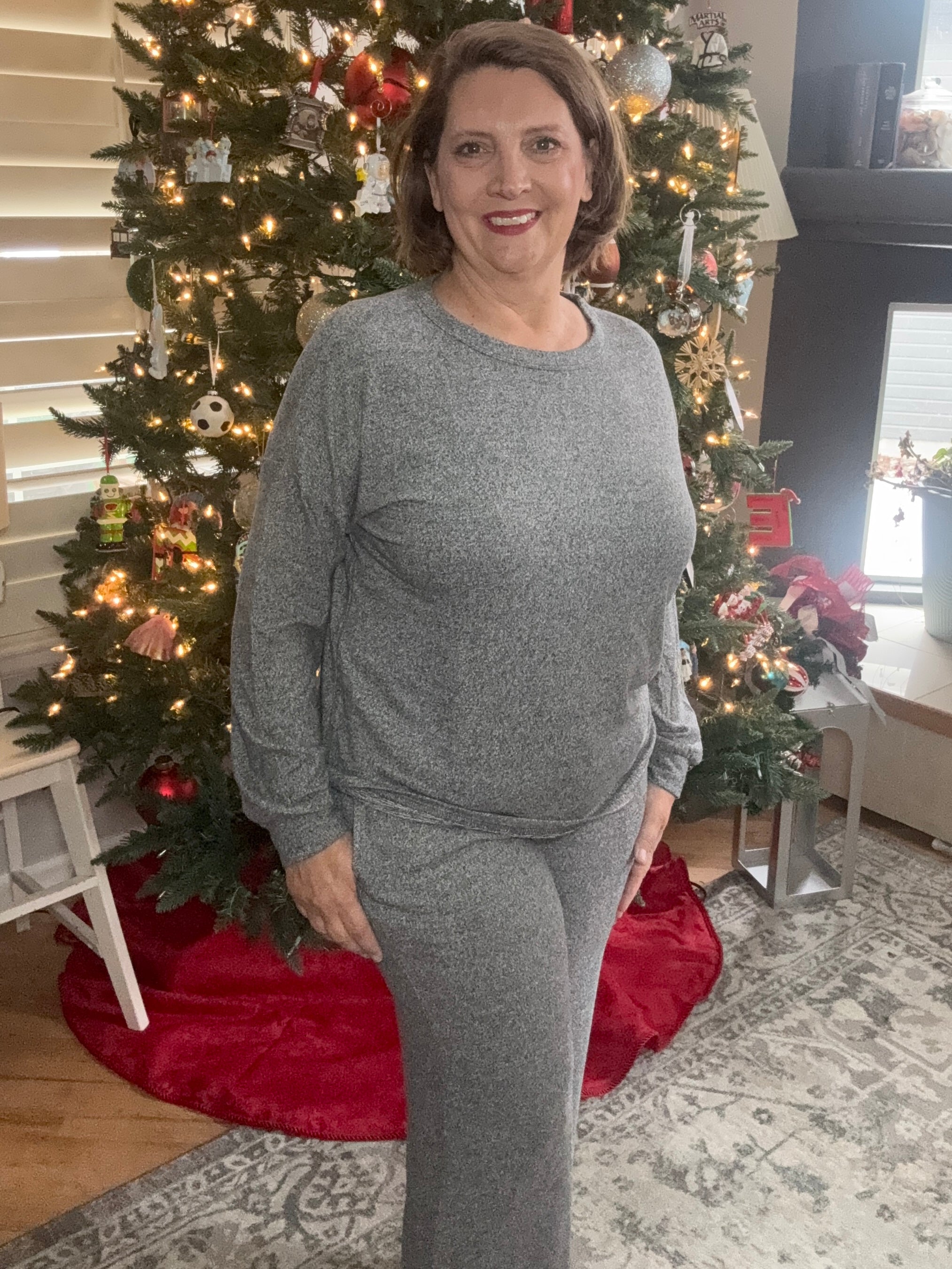 Woman in a gray outfit standing in front of a decorated Christmas tree.