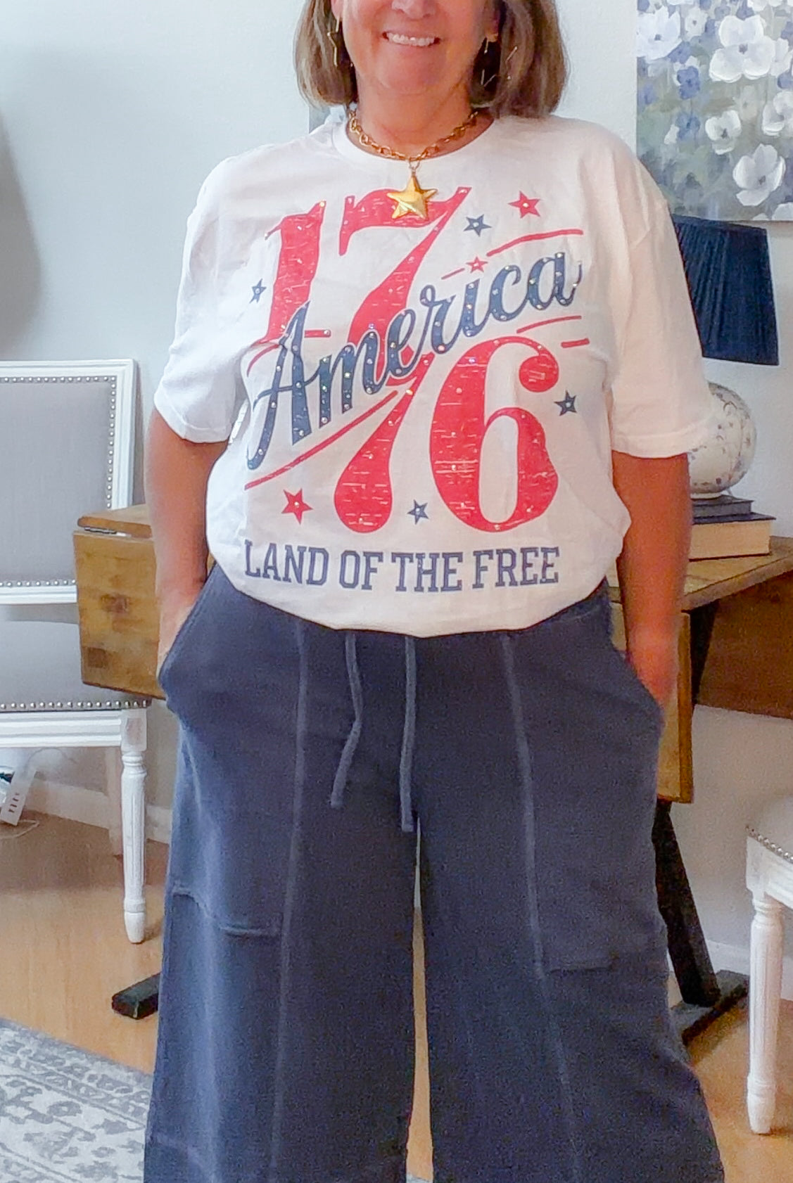 Woman wearing a white t-shirt with 'America 76 Land of the Free' text in a home setting.