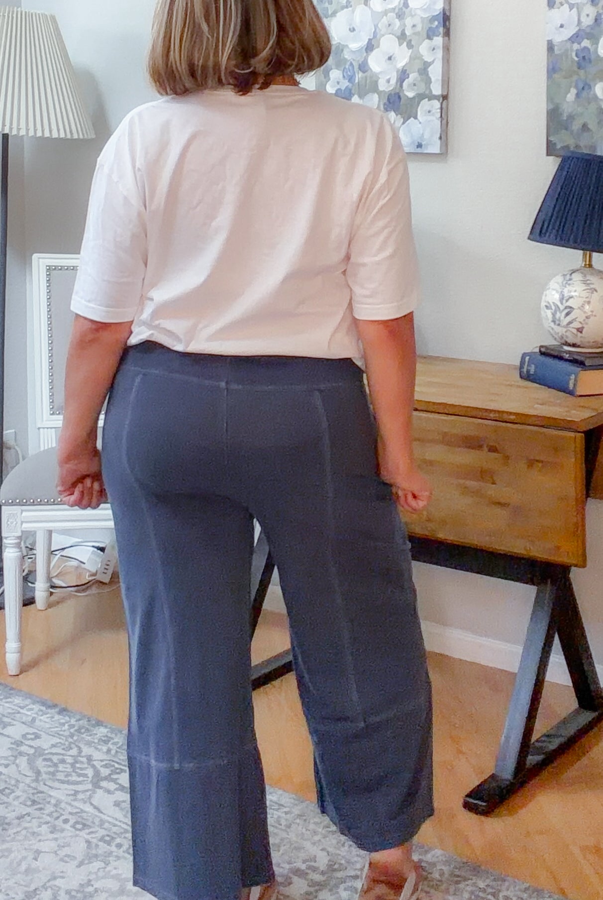 Person wearing a white shirt and blue pants in a room with a desk and lamp.