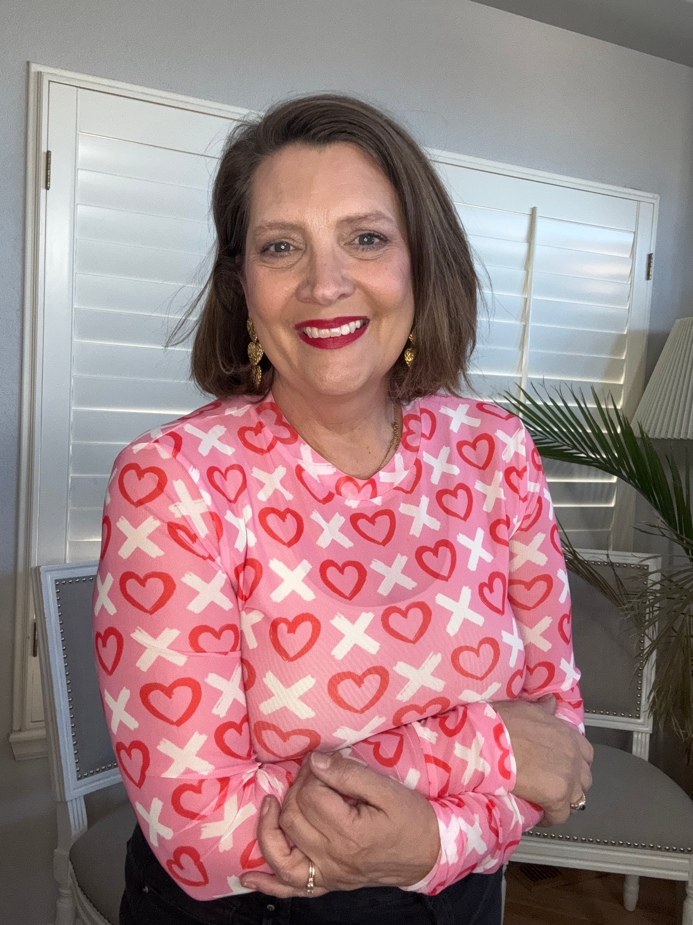 Woman wearing a pink jacket with heart and cross pattern indoors.