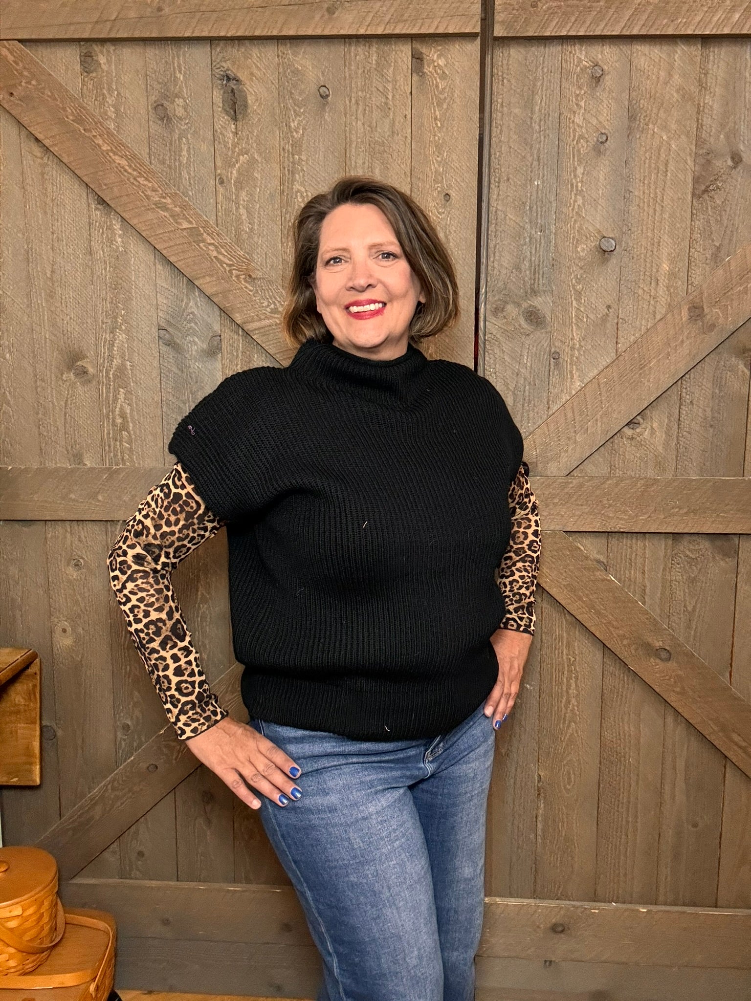 Woman wearing a black sweater with leopard print sleeves against a wooden background
