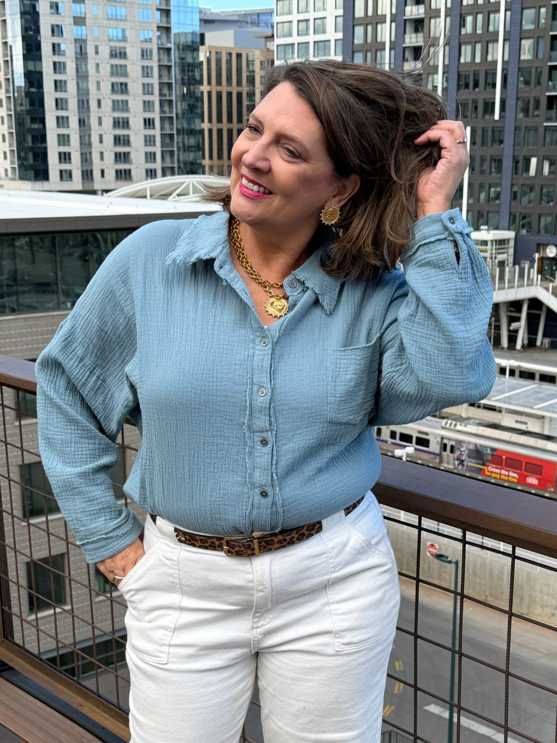 Woman in a blue shirt and white pants standing on a rooftop with cityscape in the background