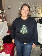 Person wearing a black sweater with a Christmas tree design in a room setting.