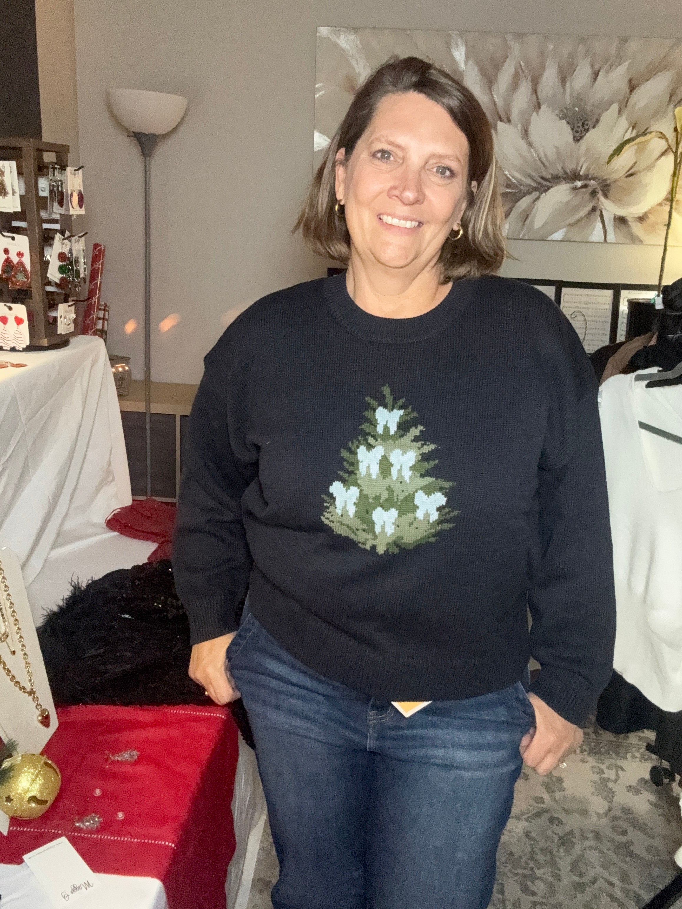Person wearing a black sweater with a Christmas tree design in a room setting.