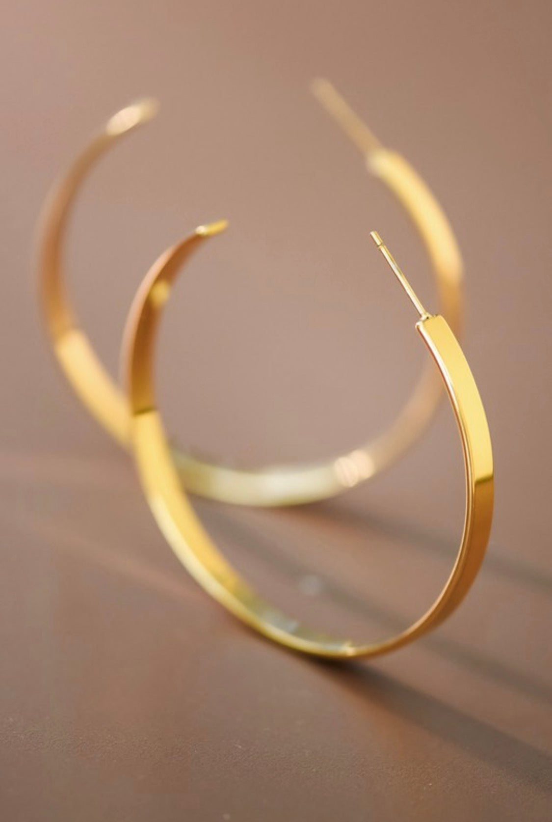 Gold hoop earrings on a reflective surface with a blurred background