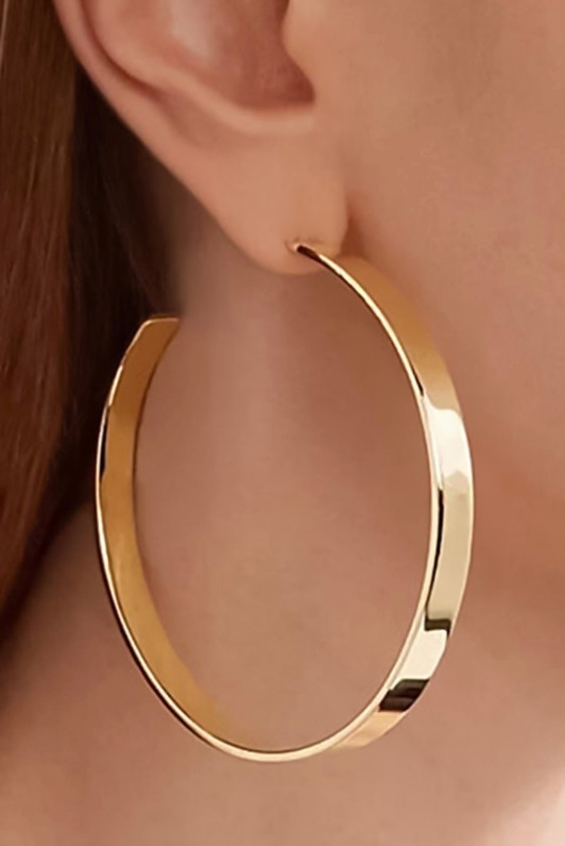 Gold hoop earring worn on an ear with a blurred background