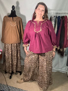 Woman standing next to a rack of leopard print pants and a maroon top on a mannequin.