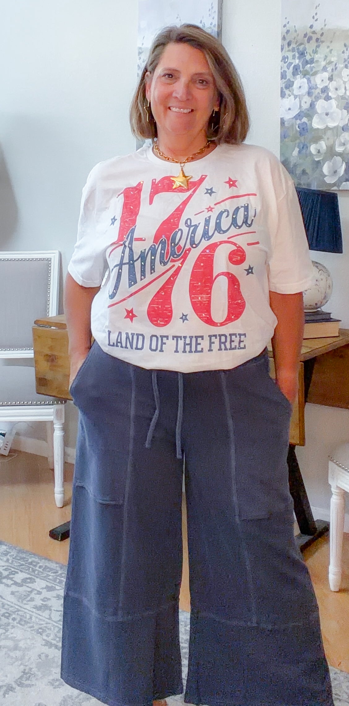Woman wearing a white t-shirt with 'America 76 Land of the Free' text in a home setting.