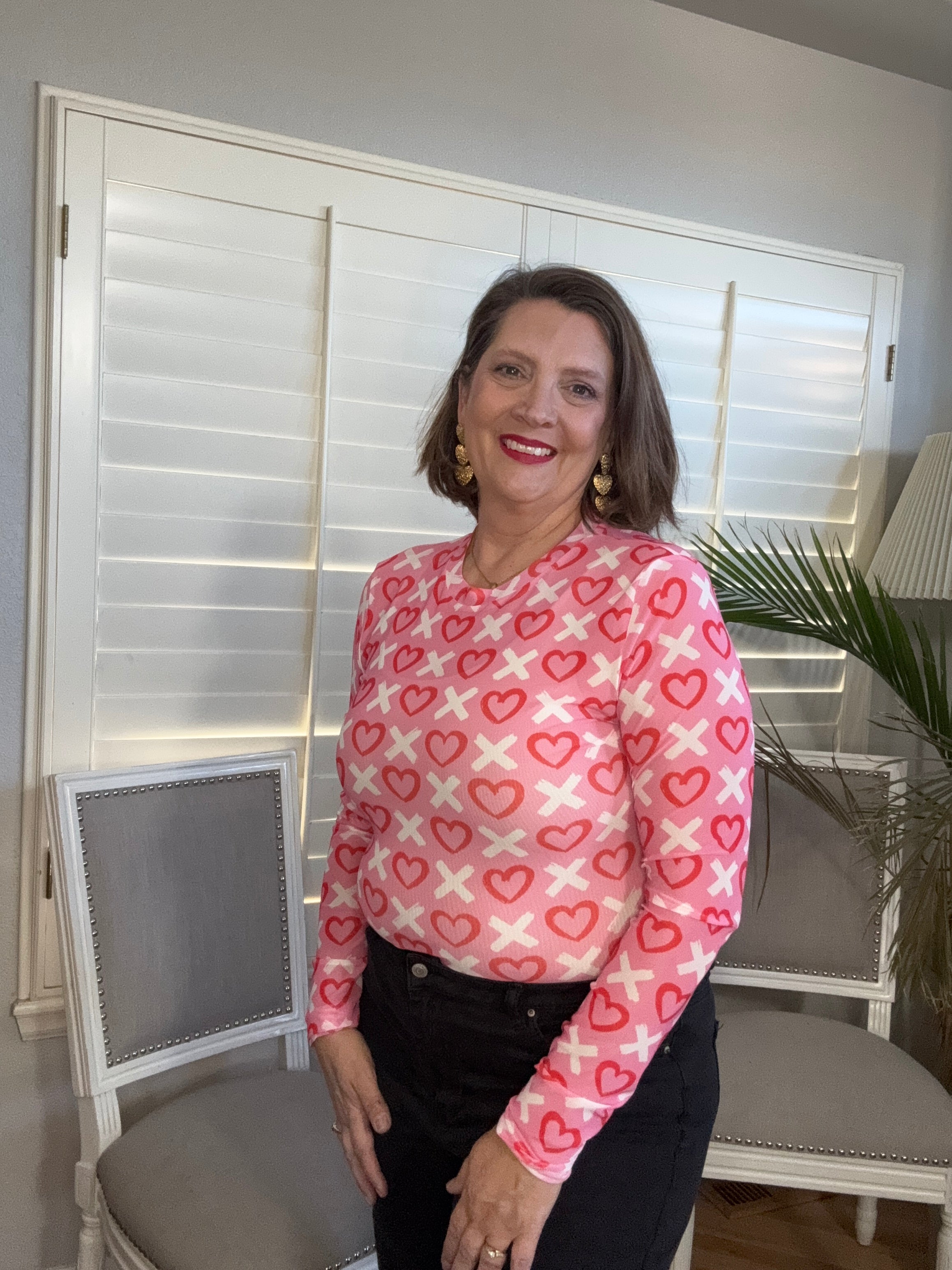 Woman wearing a pink shirt with heart patterns in an indoor setting