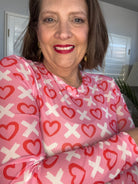 Woman wearing a pink sweater with red heart and white cross patterns.