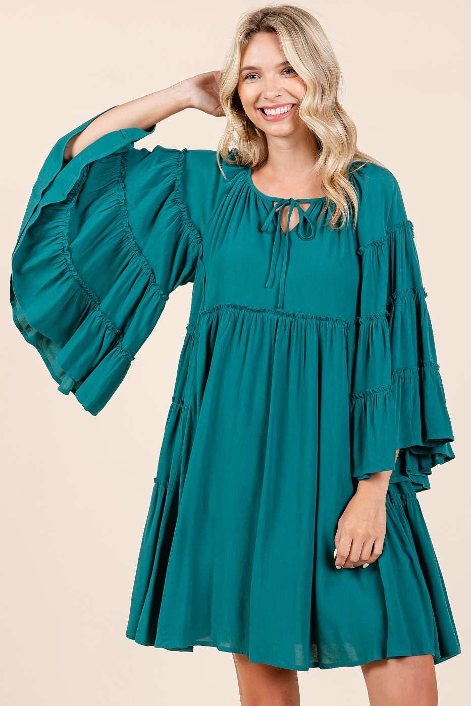 Woman wearing a teal dress with balloon sleeves on a beige background